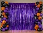 Painel decorativo de Halloween com cortina metalizada roxa brilhante utilizada como fundo para fotos e decoração temática.