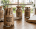 POTINHOS DE VIDRO COM VÁRIOS ROLINHOS DE PAPEL KRAFT DENTRO. NA PARTE EXTERNA, ADESIVADOS COM A MENSAGEM: XV ENCONTRO DE CASAIS COM CRISTO - MENSAGENS PARA UM DIA MELHOR