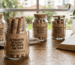 POTINHOS DE VIDRO COM VÁRIOS ROLINHOS DE PAPEL KRAFT DENTRO. NA PARTE EXTERNA, ADESIVADOS COM A MENSAGEM: XV ENCONTRO DE CASAIS COM CRISTO - MENSAGENS PARA UM DIA MELHOR