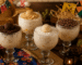 Taças de canjica cremosa decoradas com brigadeiro tradicional, beijinho, brigadeiro de paçoca e raspas de chocolate, servidas sobre uma mesa rústica decorada para festa junina