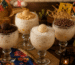 Taças de canjica cremosa decoradas com brigadeiro tradicional, beijinho, brigadeiro de paçoca e raspas de chocolate, servidas sobre uma mesa rústica decorada para festa junina