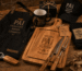 Kit contendo tábua de churrasco gravada, avental, caneca personalizada e acessórios organizados sobre uma mesa de madeira rústica. Fotografia profissional estilo Pinterest.