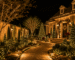 Área externa residencial completamente decorada para o Natal, com árvores iluminadas, arbustos, cascatas de LED no muro, caminho luminoso e detalhes natalinos, composição sofisticada