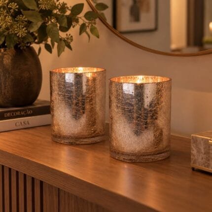 Castiçal de vidro na cor rose gold com acabamento craquelado, apresentado em uma composição decorativa elegante sobre aparador.