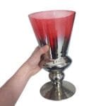 Vaso de vidro vermelho com detalhes prateados e tampa, destacando seu formato alto, elegante e imponente.
