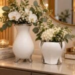 Conjunto com dois vasos decorativos de cerâmica branca e detalhes prateados, apresentado lado a lado para destacar os diferentes formatos e tamanhos.