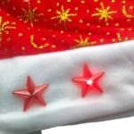 Close do tecido vermelho aveludado do gorro, destacando a textura macia e os detalhes dourados com motivos natalinos.
