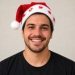 Gorro natalino vermelho confeccionado em tecido aveludado, com estampas douradas, pompom branco e estrelas de LED na faixa inferior.