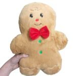 Close do rosto e do corpo da almofada Gingerbread, destacando a textura peluciada, os detalhes bordados, o laço vermelho e os elementos decorativos.