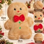 Close do rosto e do corpo da almofada Gingerbread, destacando a textura peluciada, os detalhes bordados, o laço vermelho e os elementos decorativos.